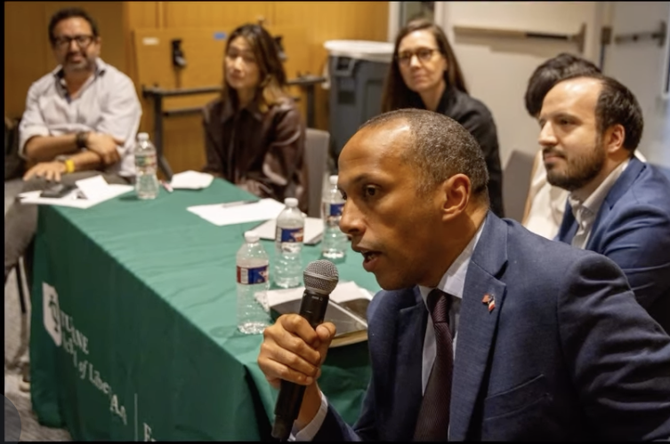 Nuit des Idees. Man speaks into a microphone at a panel discussion table with five other attendees.