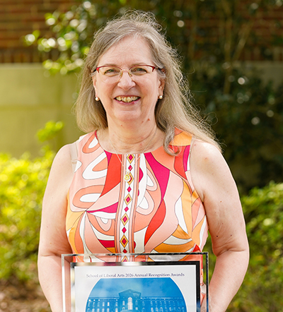 Smiling woman in a vibrant, patterned dress holds an award plaque.