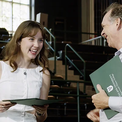 Smiling student receives green certificate from professor