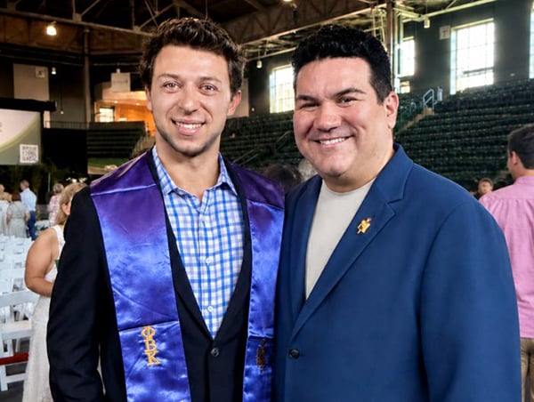 Two smiling men, one wearing a purple phi beta kappa graduation stole, at a formal indoor event.