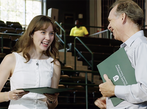 Smiling woman receives a green document from a man in an auditorium.