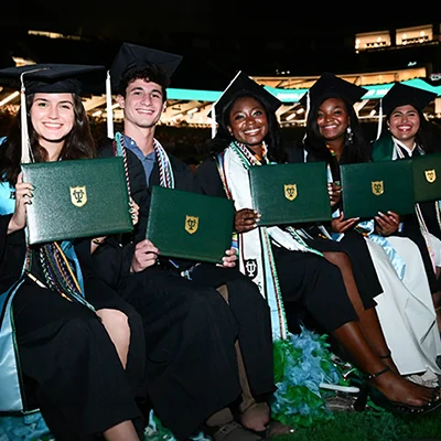 Smiling Tulane graduates in caps and gowns hold diplomas.
