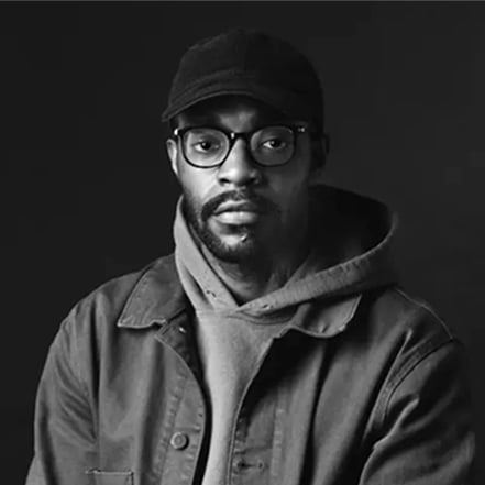 Black and white photograph of a man in a cap, glasses, and jacket.