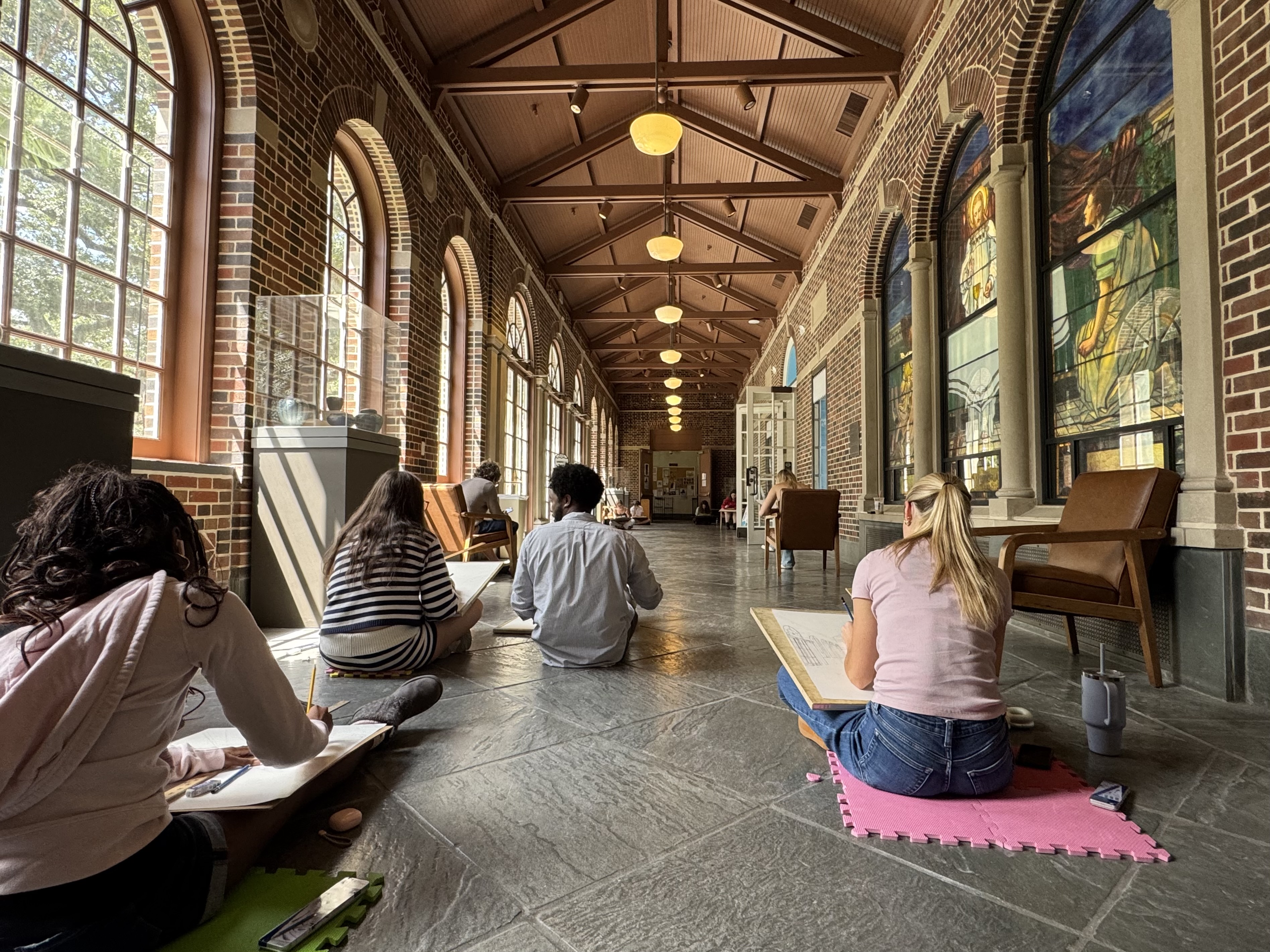 students seated on the floor learning perspectice drawing in Woodward Way by the Tiffany stained gla