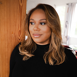 Portrait of woman wearing a black top leaning against a woodgrain backdrop