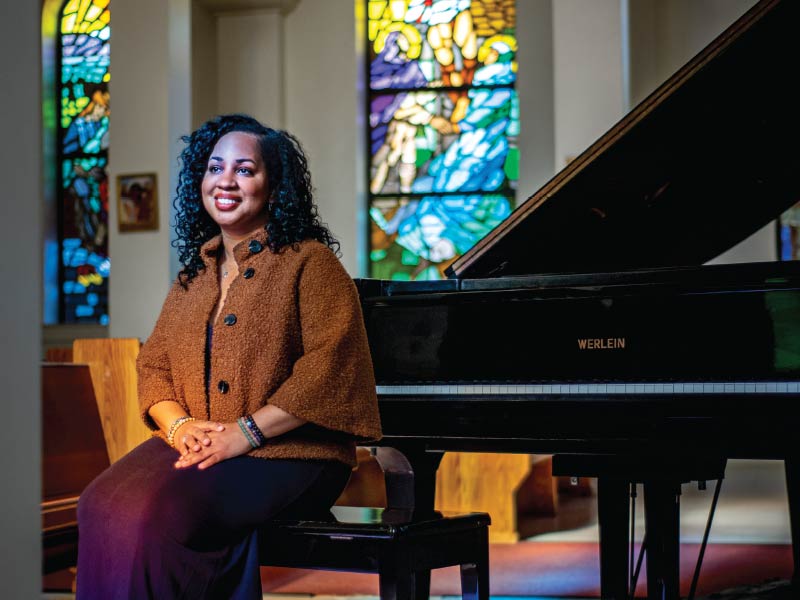 Courtney Bryan sitting at a grand piano underneath stain glass windows