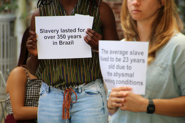 People hold signs showing facts about slavery in Brazil