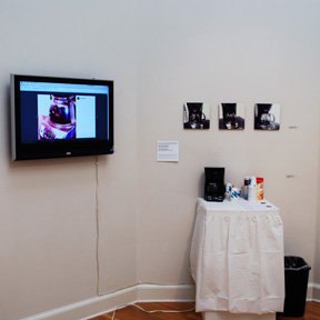 installation view of coffeepot with its own Instagram account, on small table with cream and sugar, and video monitor of coffeepot's social media account