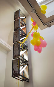 five steel and neon squares hung up high on wall with yellow and pink balloons