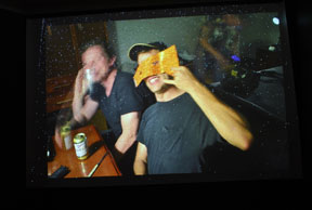 video still with two men sitting at a table and smiling with beer cans on table
