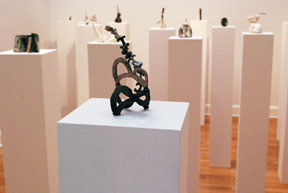 grouping of ten pedestals with one pedestal in front supporting a black linear ceramic sculpture