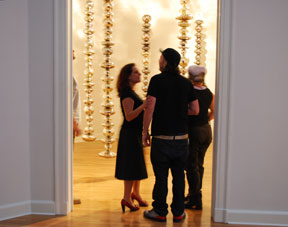 three people standing in doorway, backlit by gallery light with hanging glass sculptures behind them