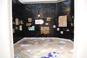 view of gallery with plastic on walls, cardboard on floor, and pizza boxes attached to wall