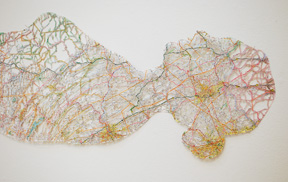 detail of head and chest of reclining figure made of road maps with blank areas removed, creating a lace-like structure