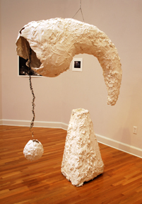large horn-like hollow form suspended from ceiling with pyramidal pedestal beneath