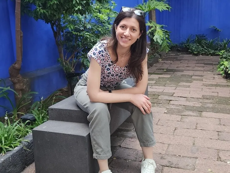 Sara Panteri sitting down with a blue background and trees